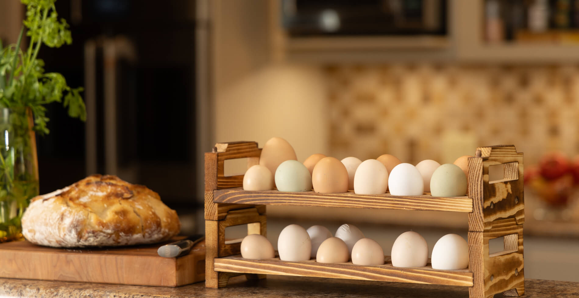 A counter with a wood block and a loaf of freshly baked bread on it, and a double wooden egg rack filled with fresh farm eggs in various colors.
